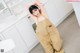 A woman in a beige overalls leaning against a white counter.