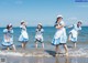 A group of young women in blue and white dresses on the beach.